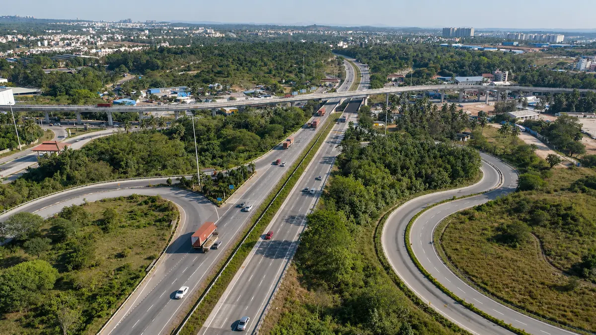 Aerial view of a divided highway interchange, with curving on- and off-ramps looping away from the main carriageway and an elevated viaduct crossing behind